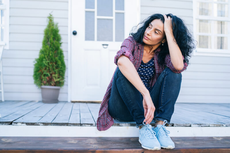 Sad mid adult woman sitting on stairs in front of her house