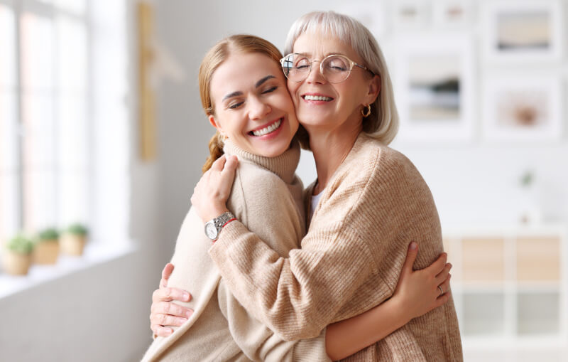 Delighted adult and senior women smiling with closed eyes and hugging each other