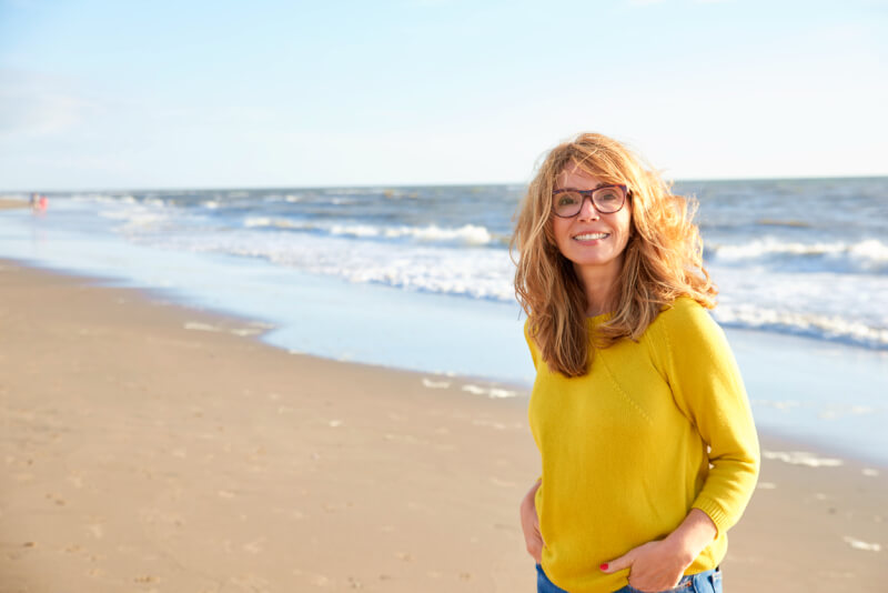 Portrait shot of beautiful smiling woman wearing sweater and jeans while relaxing on the beach