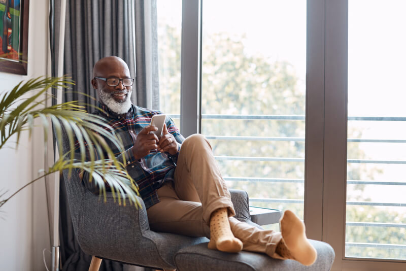Shot of a mature man using a cellphone while relaxing on a sofa at home